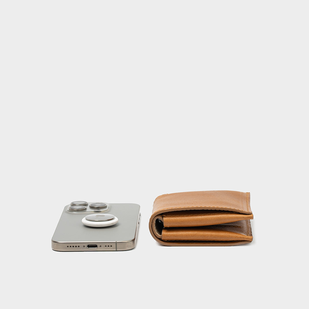 Side view of cognac brown leather wallet with built-in AirTag holder near iPhone