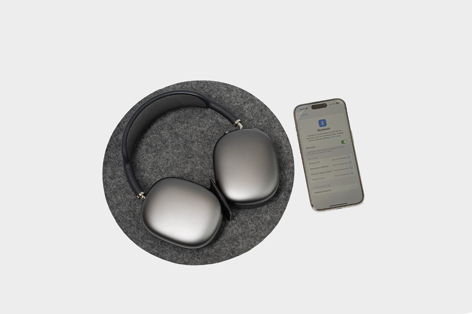 AirPods Max on grey felt rest station 2.0 with iPhone showing Bluetooth sleep mode activation – headphone dock with power saving