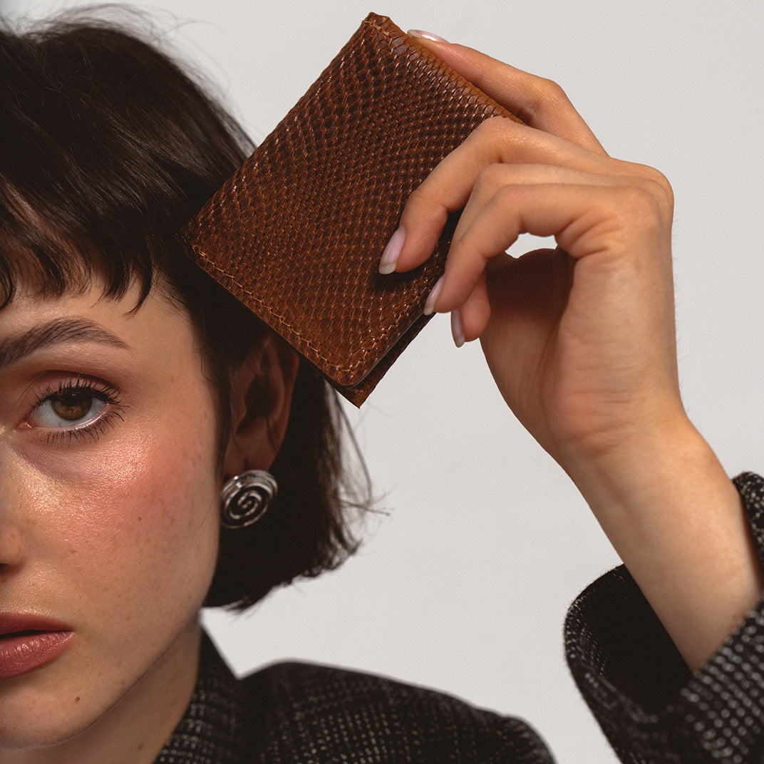 AirTag wallet - Leather AirTag Card Wallet in snake print held up by a woman in a black blazer