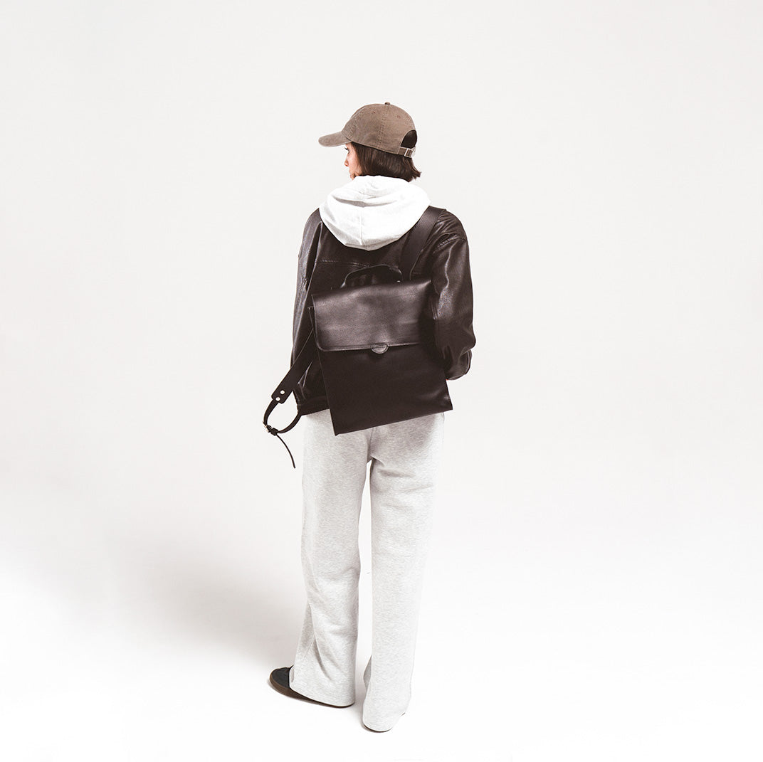 Leather backpack for woman carried by a trendy young woman in a leather jacket and cap, showing off the elegant design from the back.