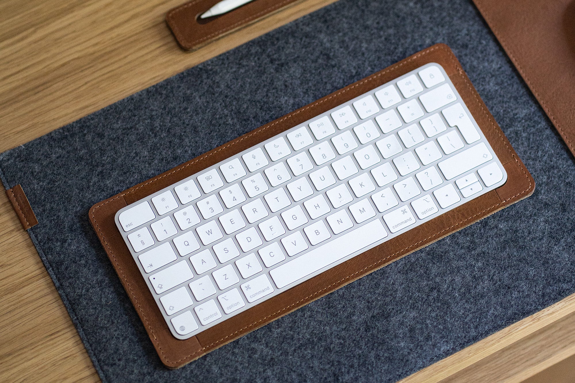 Apple Magic Keyboard in a brown leather tray on a grey felt desk pad.