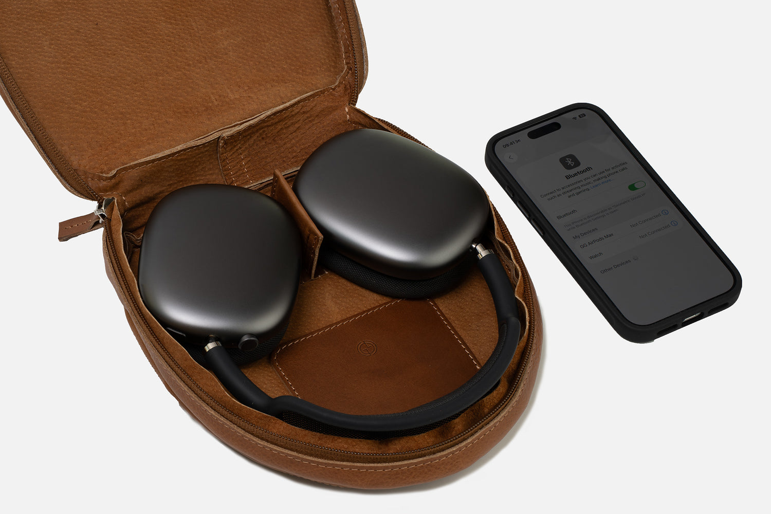 Open tan leather case for AirPods Max—headphones inside with iPhone; internal magnets trigger Low Power Mode, soft lining and interior cable pocket