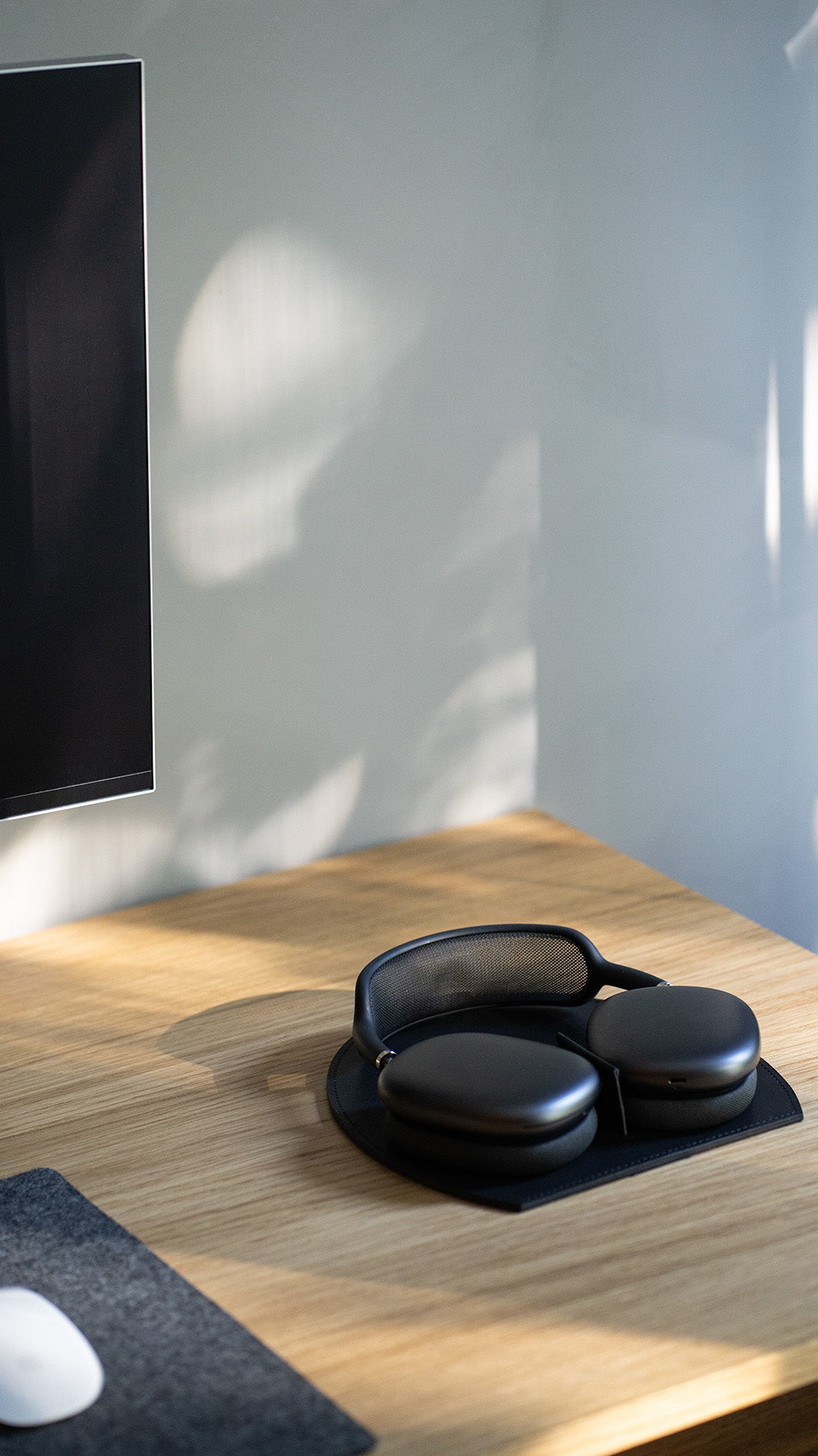 AirPods Max on a black leather rest station on a wooden desk; magnetic tab triggers low-power mode.