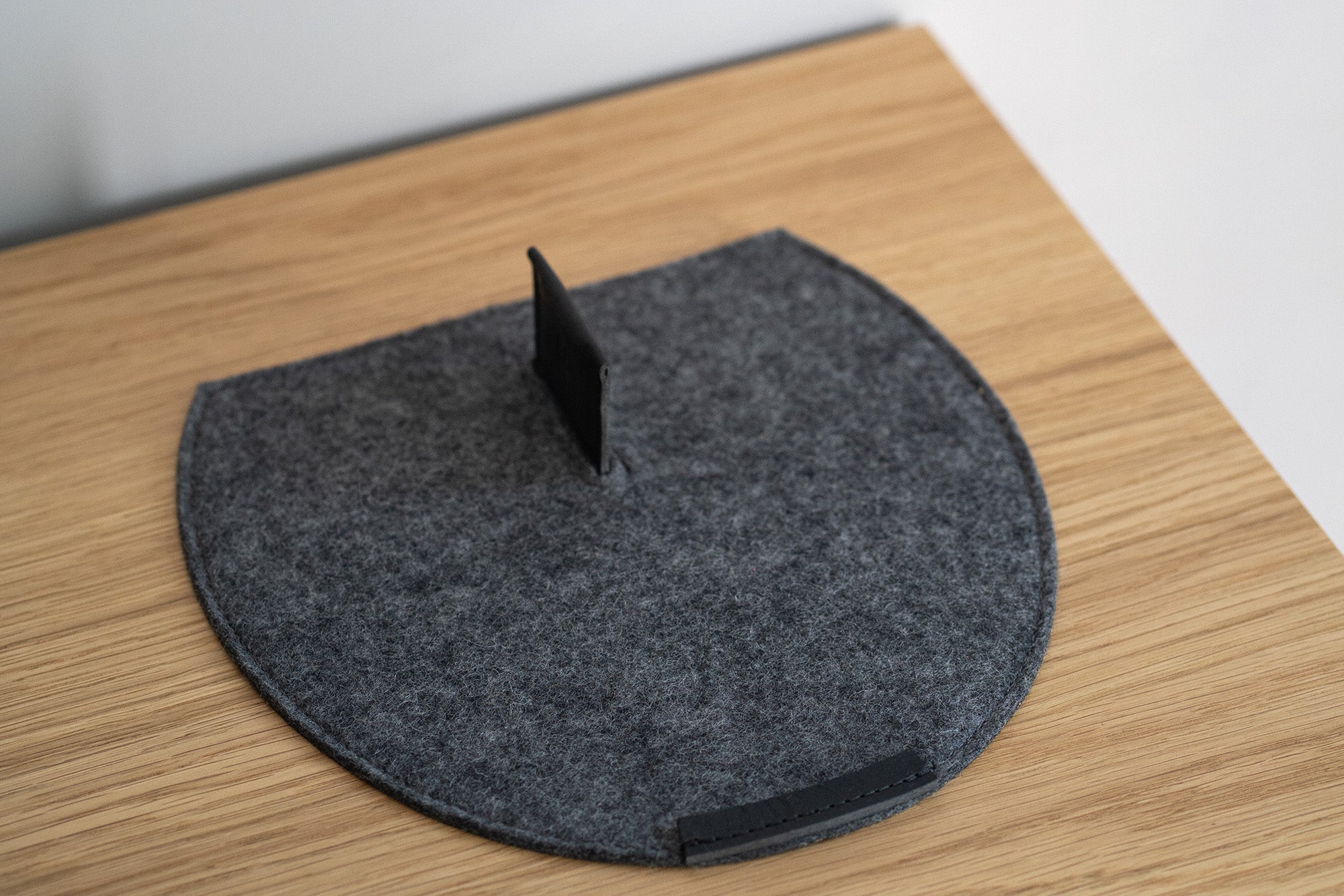 Grey wool felt AirPods Max rest station with black leather magnetic tab and cable pass-through on a wooden desk
