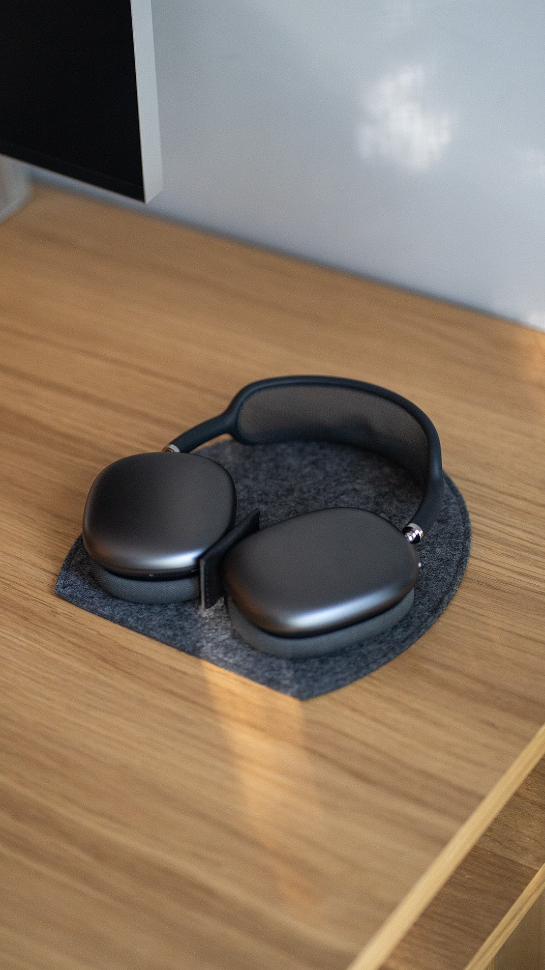 AirPods Max on a grey wool felt rest station with a leather magnetic tab on a wooden desk