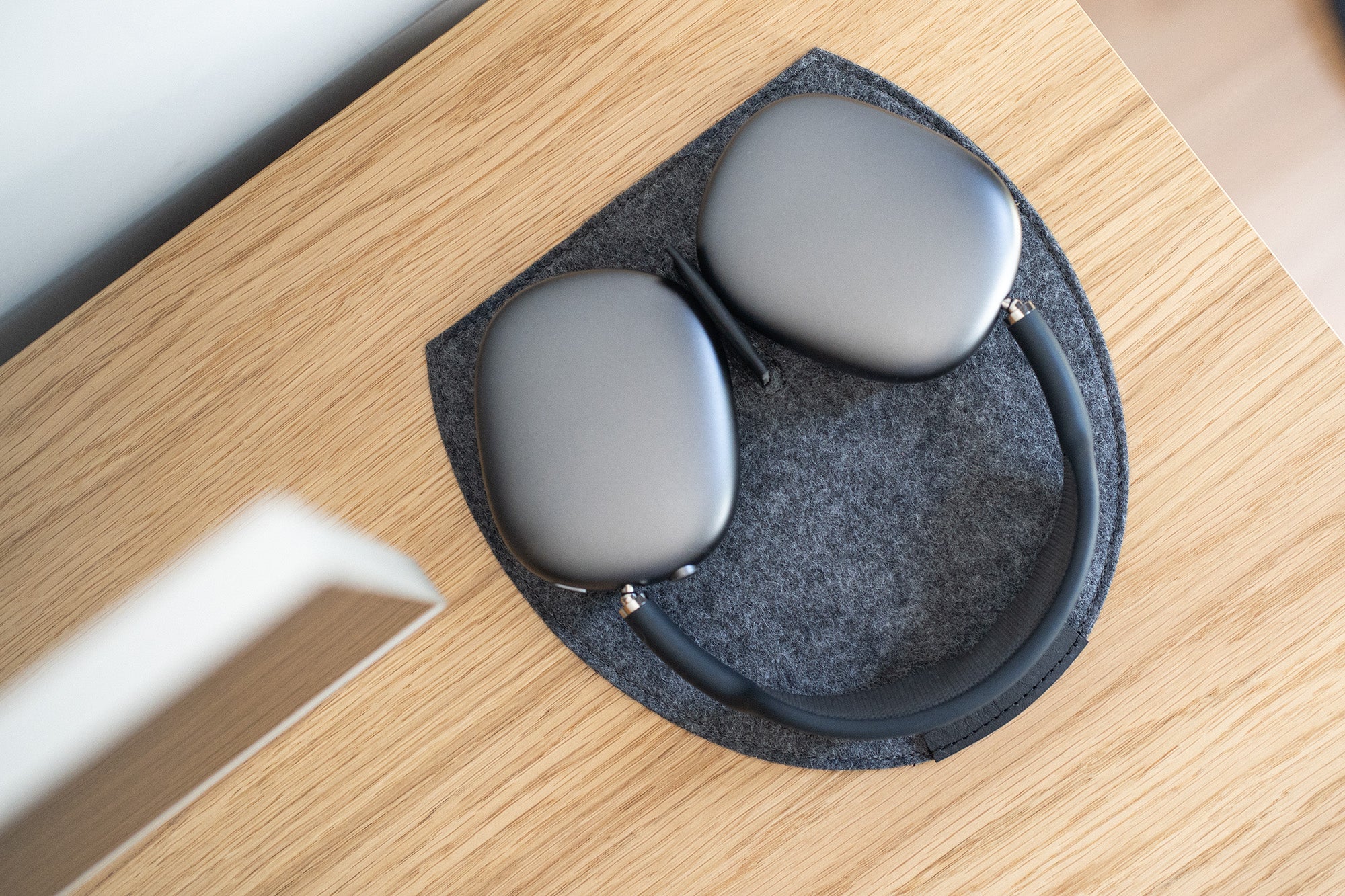 AirPods Max on a grey wool felt rest station with a leather magnetic tab on a wooden desk.