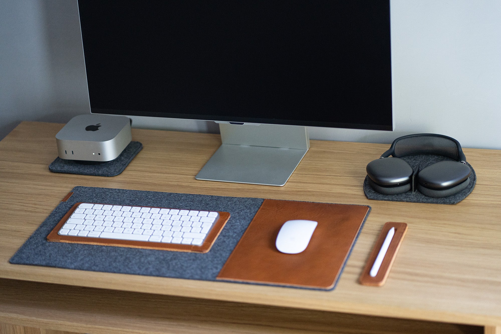 AirPods Max on a grey wool felt rest station beside a monitor; felt desk pad with leather mouse area