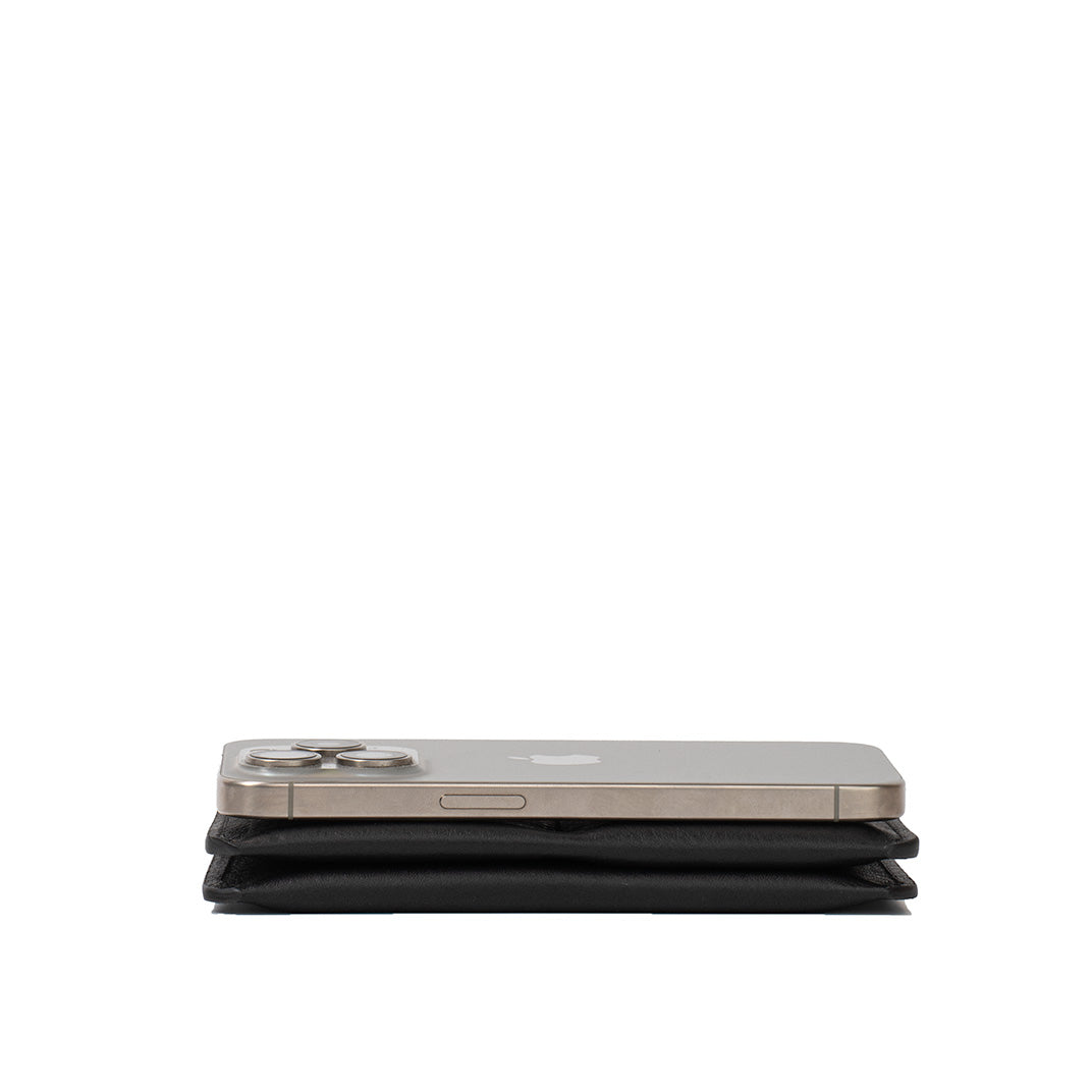 Side view of a black leather Passport Holder 2.1 for AirTag beneath an iPhone for size comparison