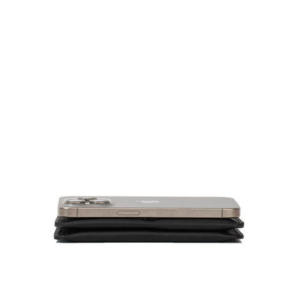 Side view of a black leather Passport Holder 2.1 for AirTag beneath an iPhone for size comparison