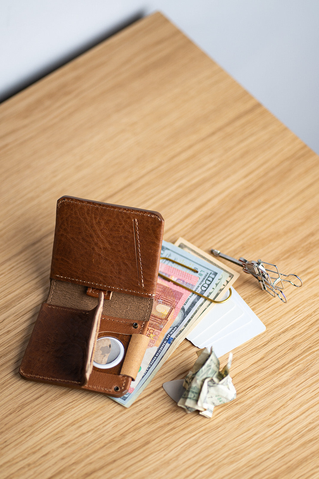 Leather bilfold AirTag wallet with cash and mixed banknotes.