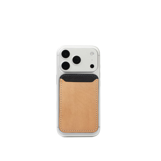 Beige and black leather MagSafe wallet attached to the back of a silver iPhone with one black card visible