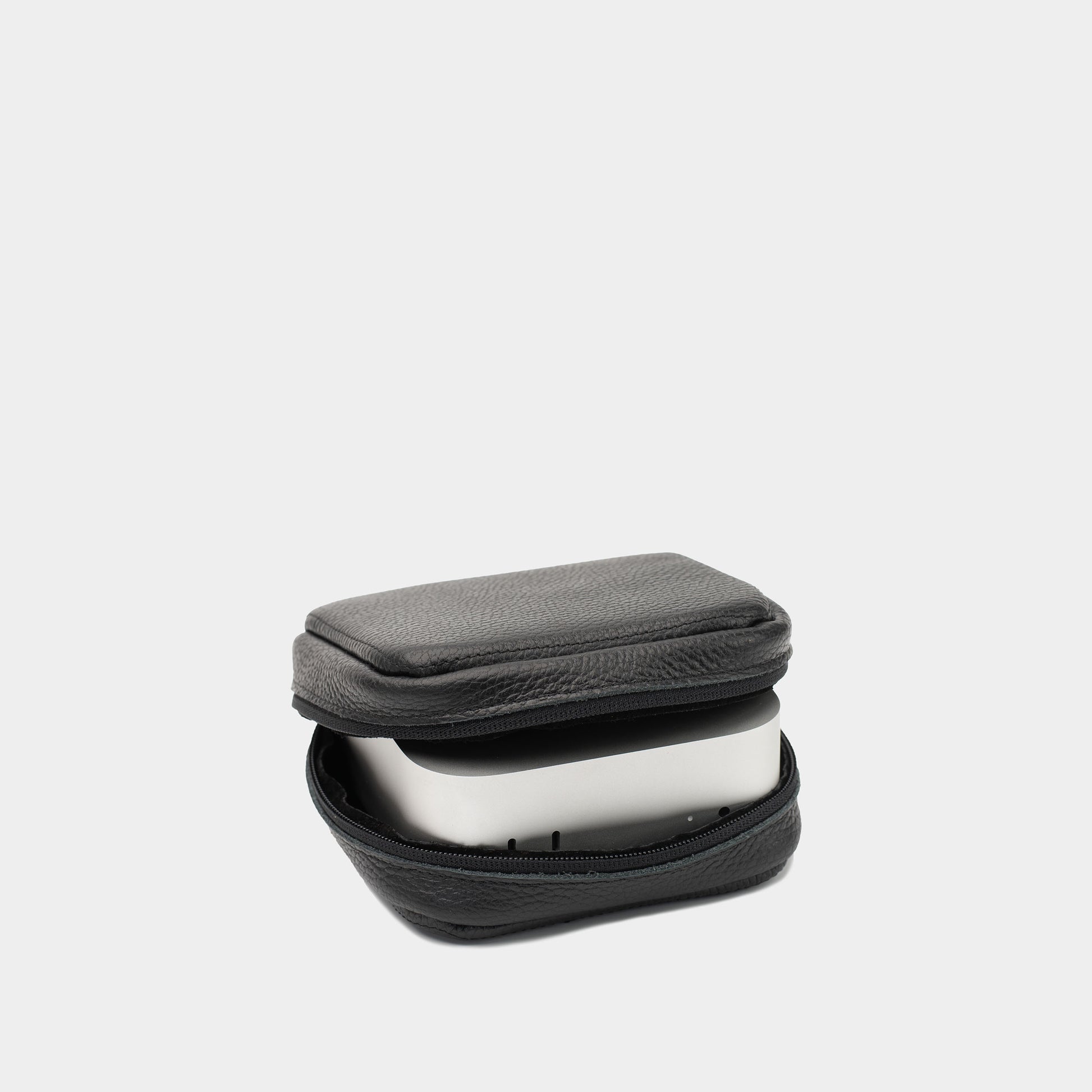 Angled view of black flat-grain leather Mac Mini case partly open with the device inside