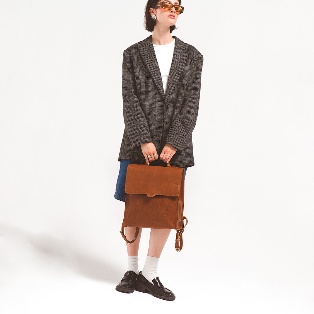 Leather backpack for woman held by a stylish woman in a herringbone blazer and sunglasses, showcasing the environmentally-friendly leather design