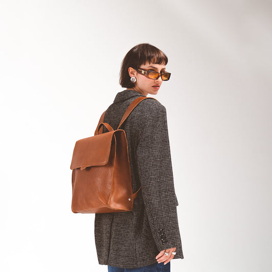 Leather backpack for woman worn by a chic young woman in a herringbone blazer and sunglasses, featuring a classic brown leather design