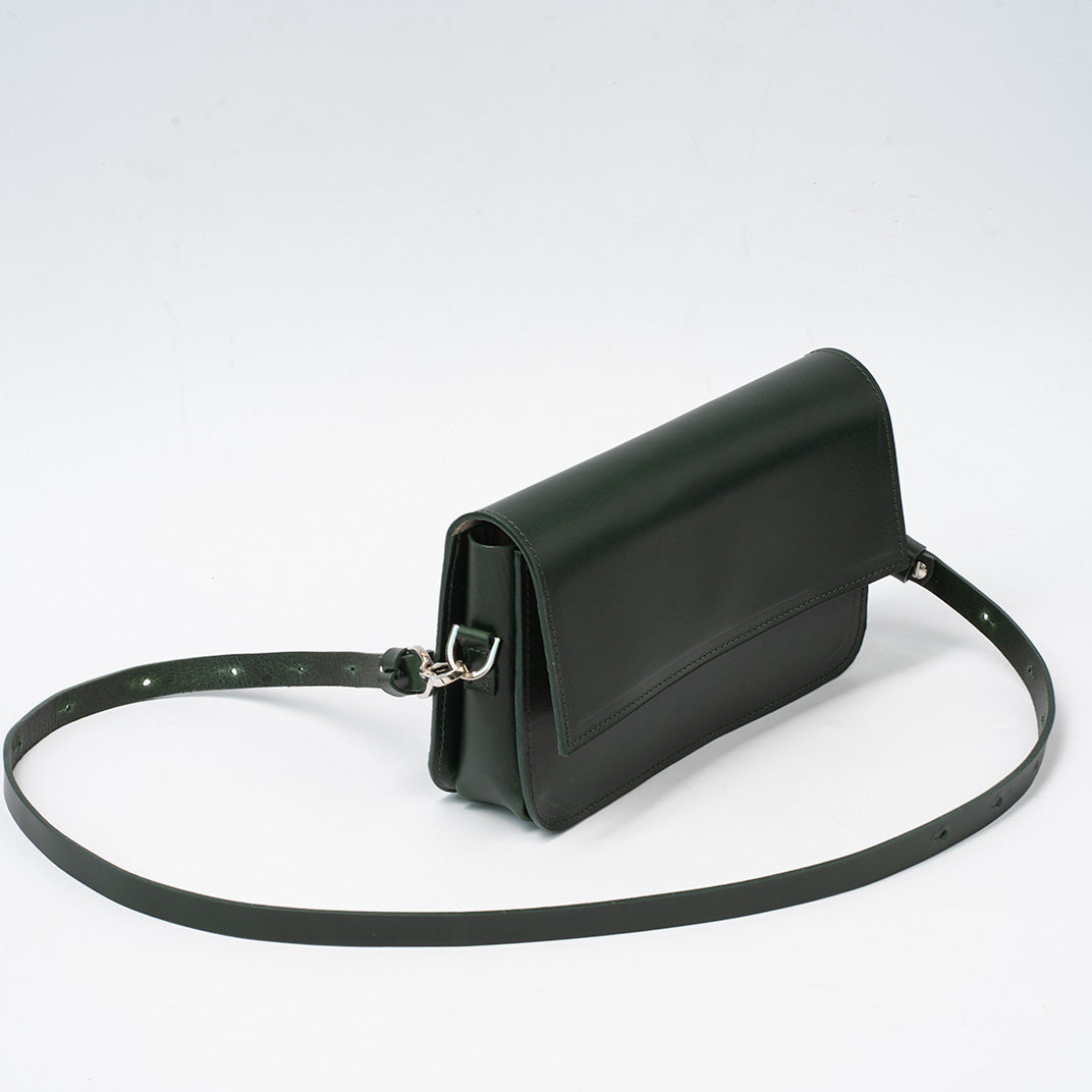 Dark green leather shoulder bag with adjustable strap and sleek minimalist design lying flat