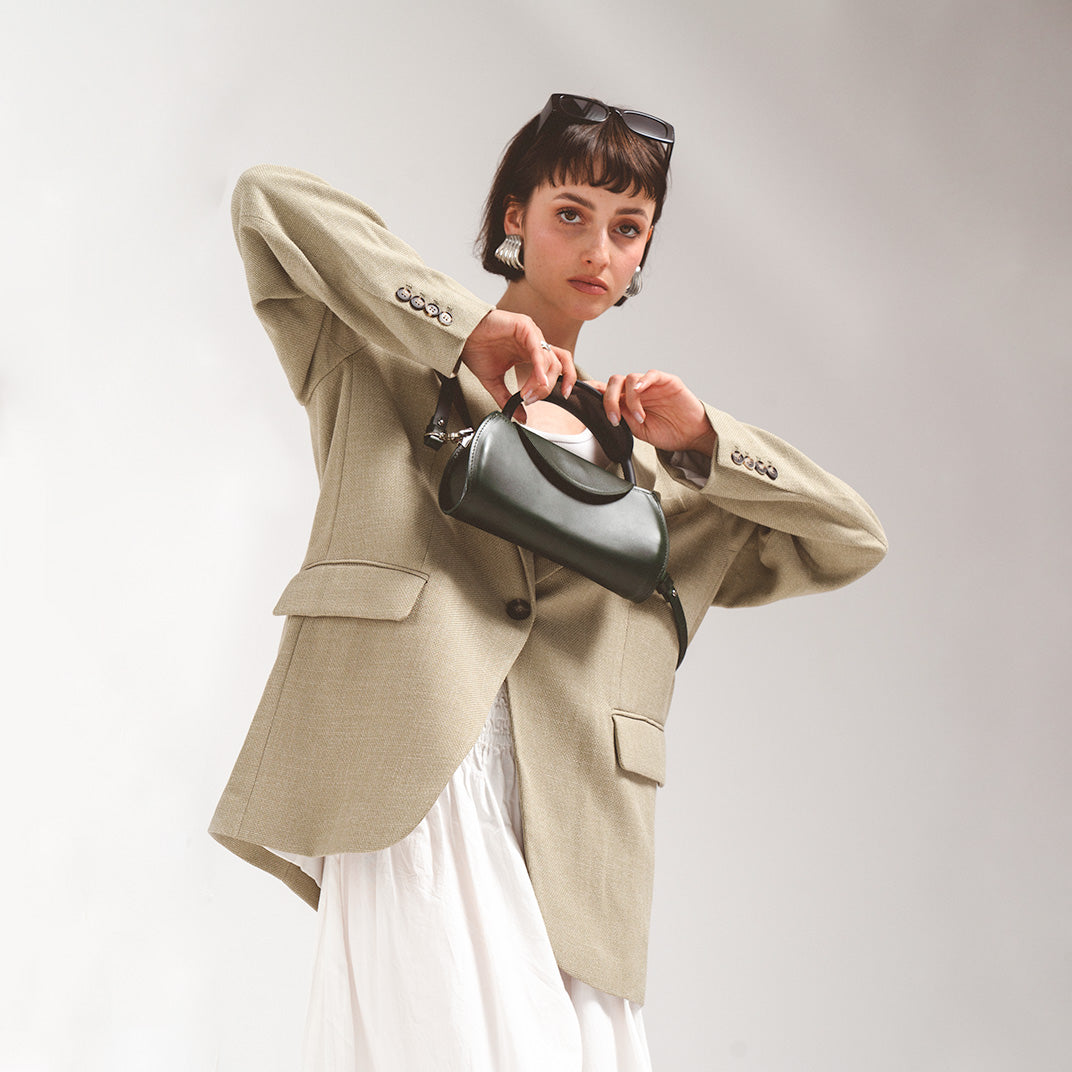 Leather case for AirPods Max in rich green, held by a fashionable woman in a beige blazer, enhancing her sophisticated look.