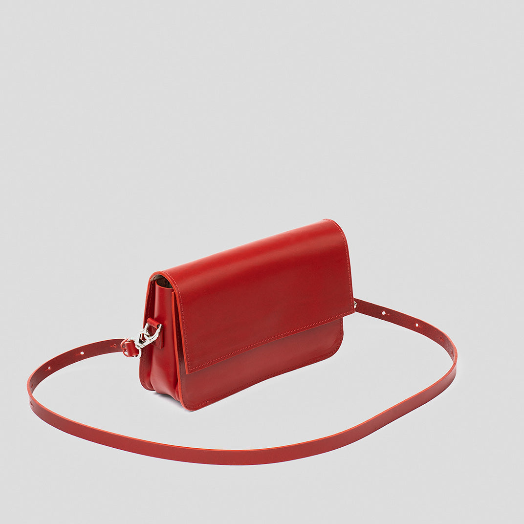 Red leather fashion shoulder bag with adjustable strap and sleek minimalist design lying flat