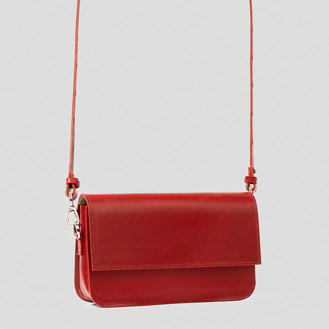 Minimalist red shoulder bag with minimalist design, displayed with strap extended