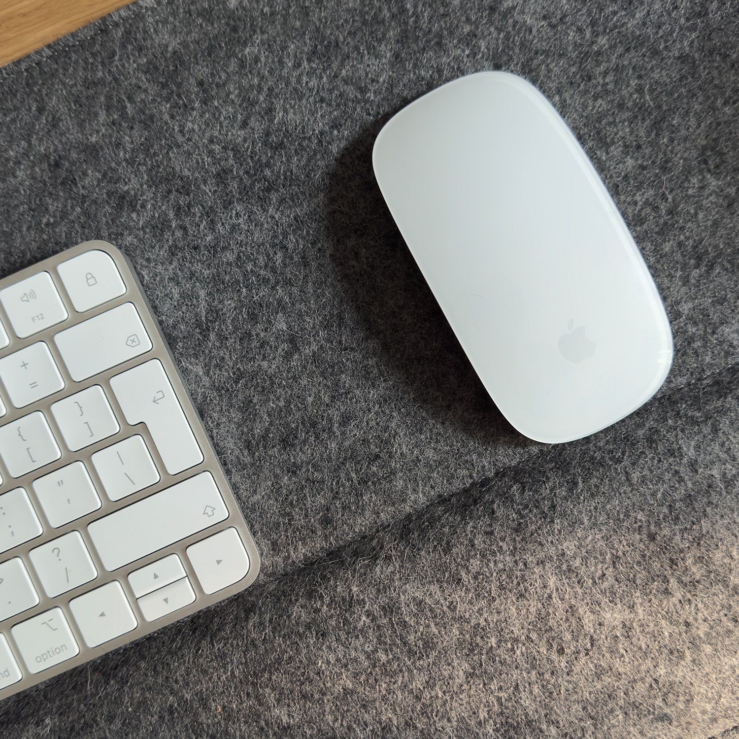 Close-up of dark wool felt desk mat with padded wrist support, Apple Magic Mouse, and keyboard