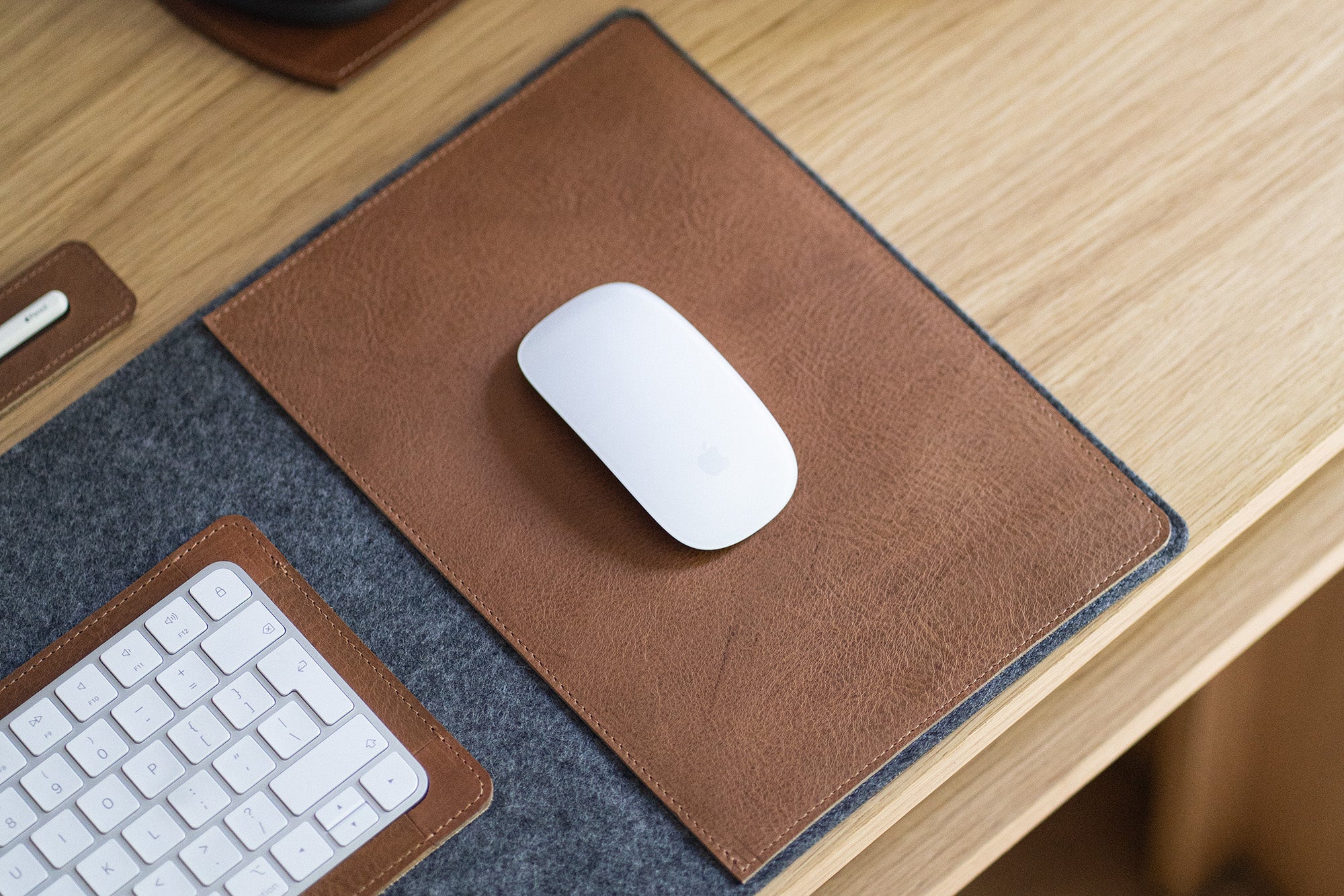 White Magic Mouse on the brown leather mouse insert of a grey felt desk pad; keyboard edge visible.