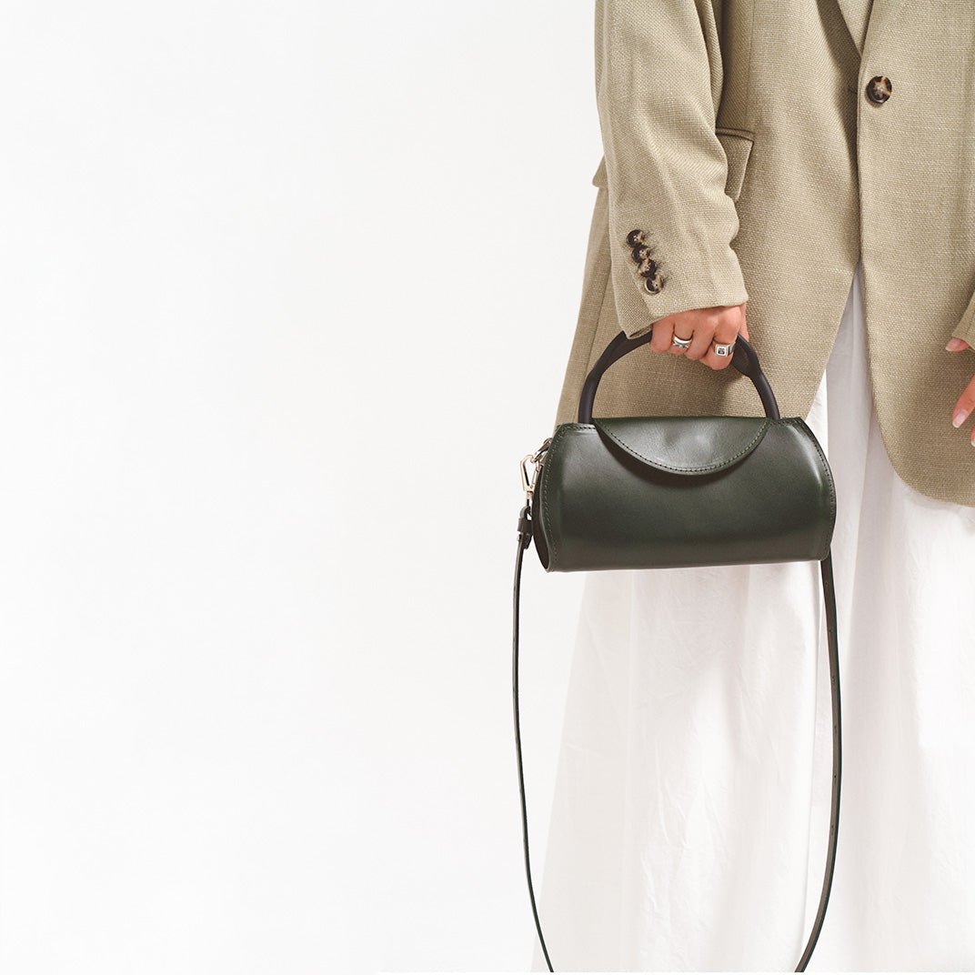 Leather case for AirPods Max in dark green, elegantly displayed by a woman with a beige blazer, highlighting the adjustable strap feature