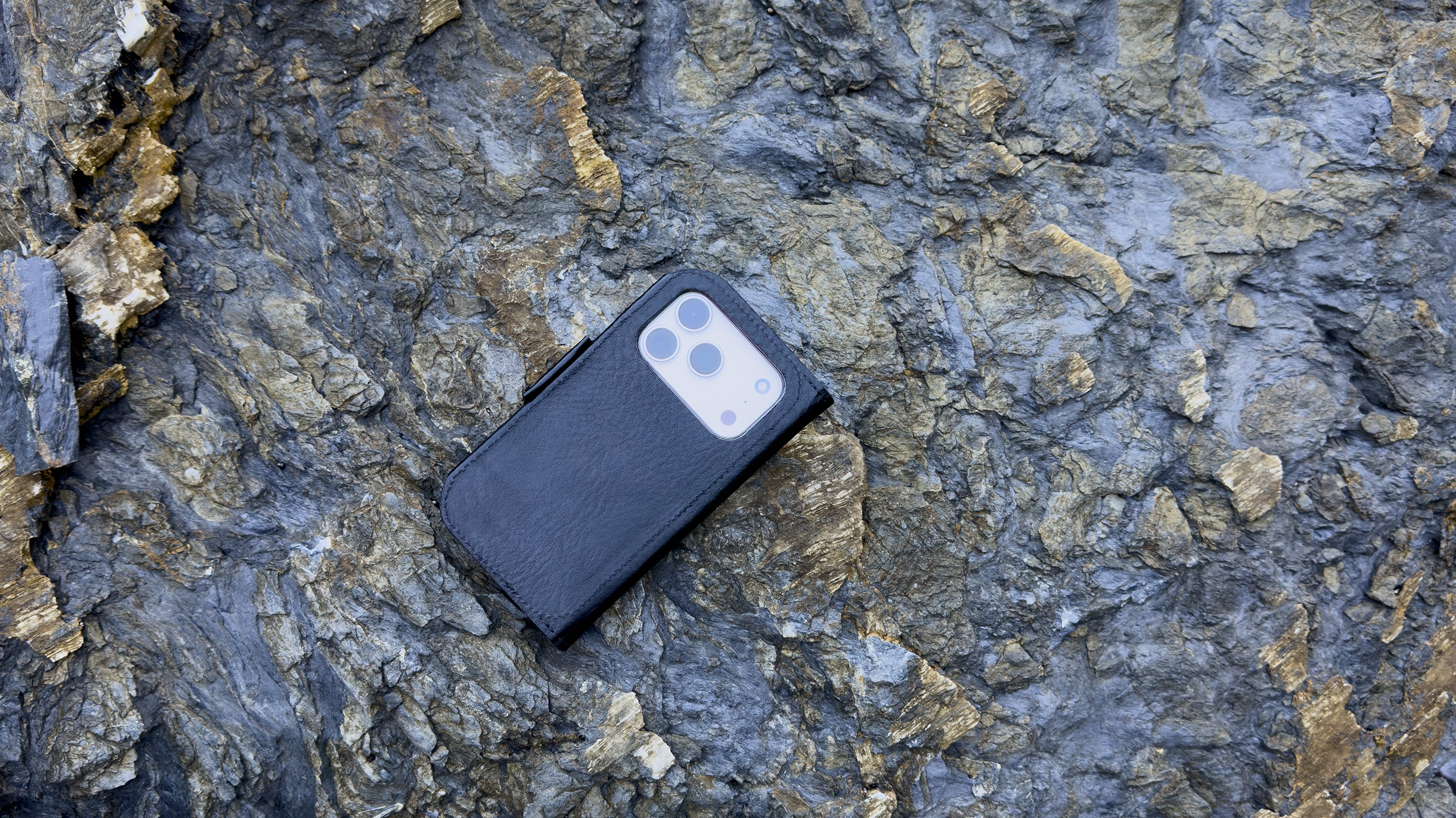 Classic 5.0 leather folio case wallet for iPhone 17 Series in black — closed view on rocky backdrop; full-grain Italian leather, MagSafe-ready