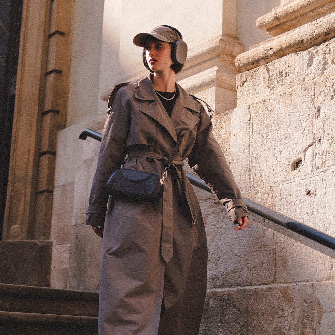 Leather case for AirPods Max in black, worn by a fashionable woman in a trench coat and headphones, exploring an urban setting