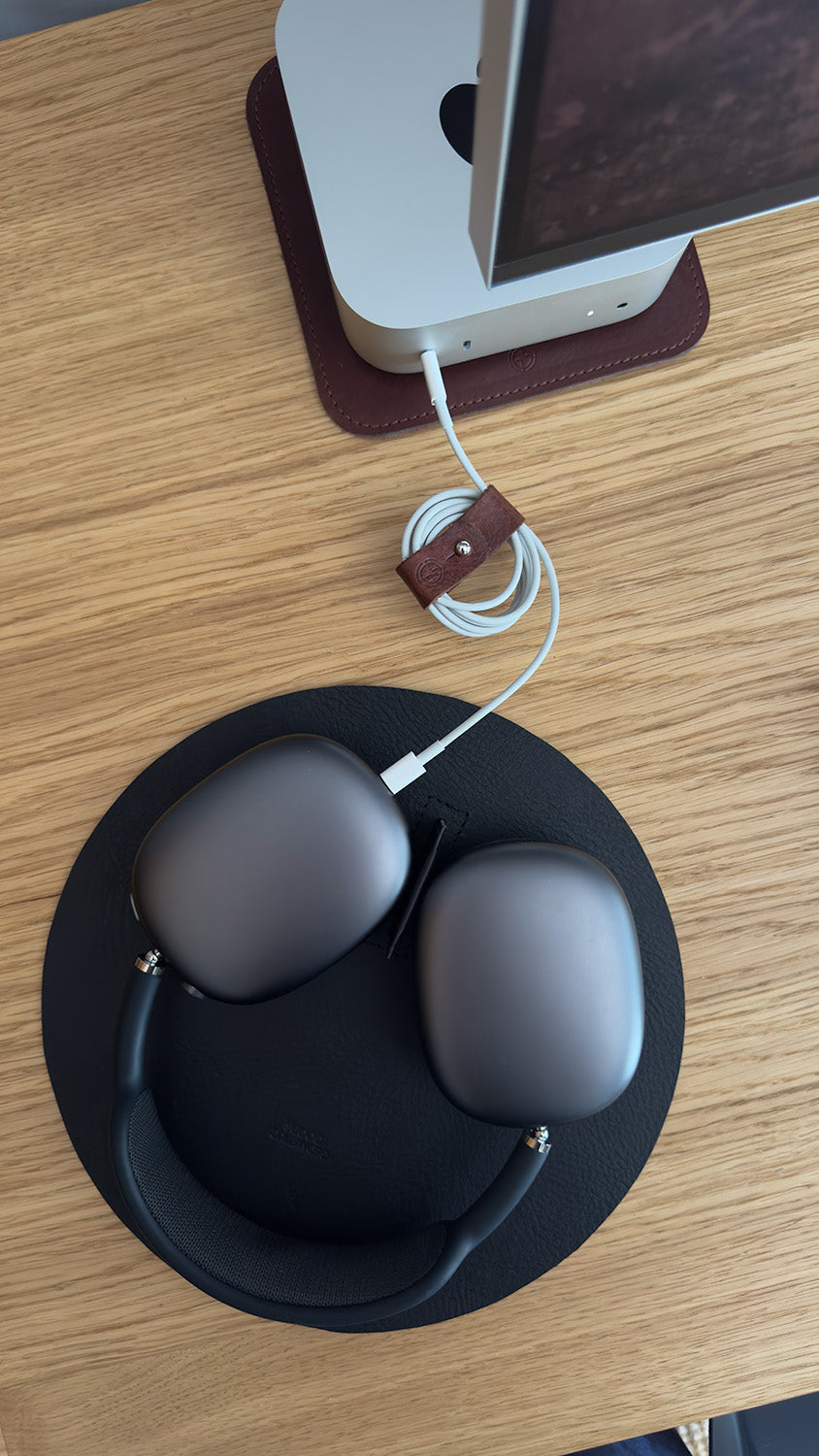 Leather cord organizer securing USB-C cable beside Mac mini, with AirPods Max and charging setup on desk