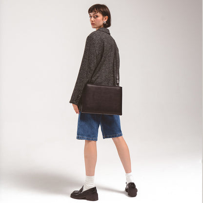 Leather iPad slim sleeve with adjustable strap, shown on a woman in a grey checkered blazer and denim shorts, highlighting its sleek design and practicality.