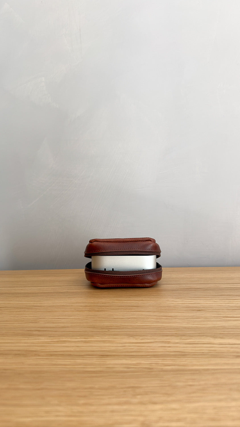 Mac Mini partially enclosed in mahogany leather case on wooden desk, front ports visible in open view