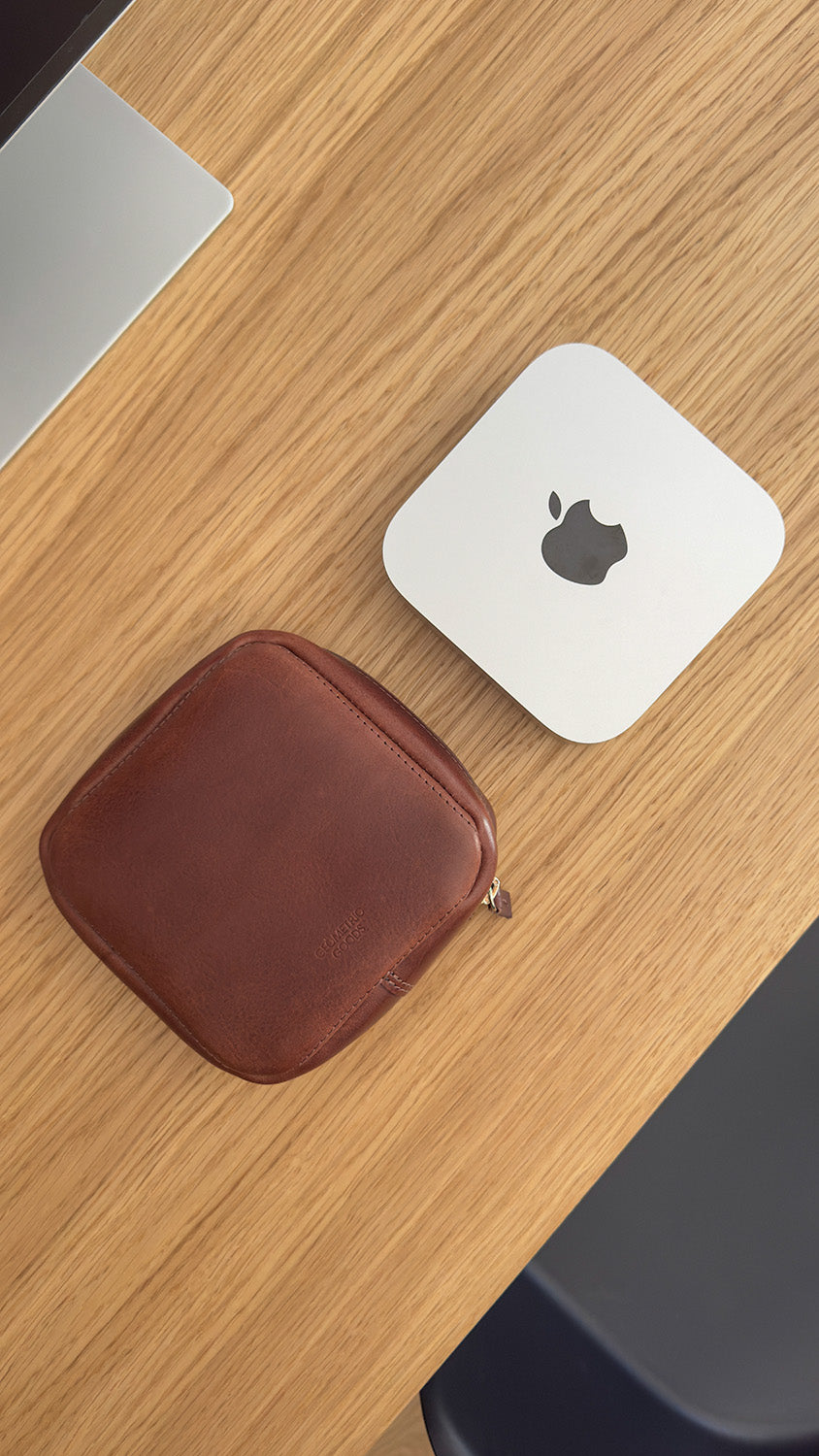 Mahogany color leather Mac Mini travel case placed beside Apple Mac Mini on wooden desk, handcrafted for protection and style
