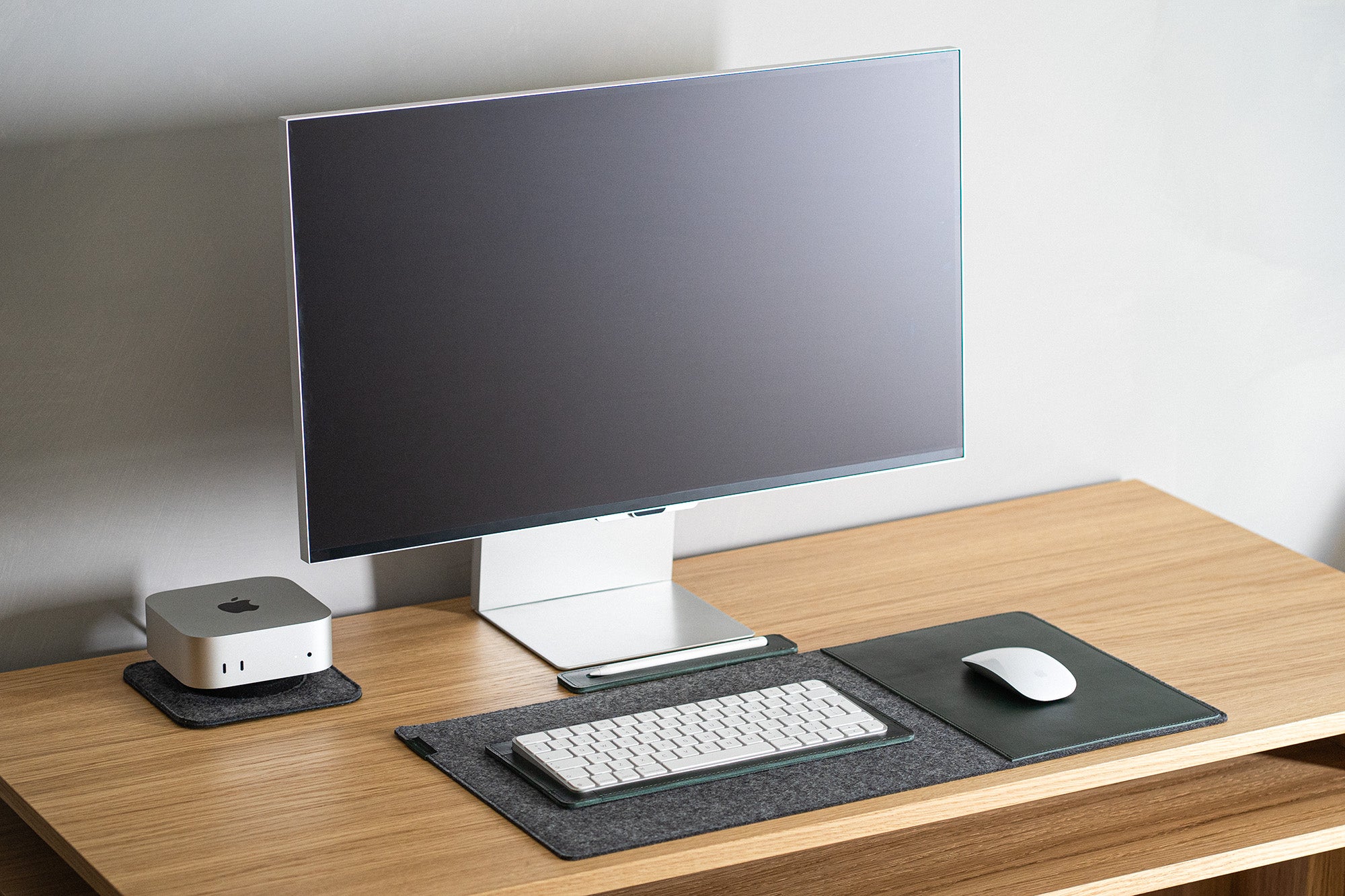 Apple Magic Keyboard in a deep green leather tray on a grey felt desk pad; matching green leather mouse area beside a monitor