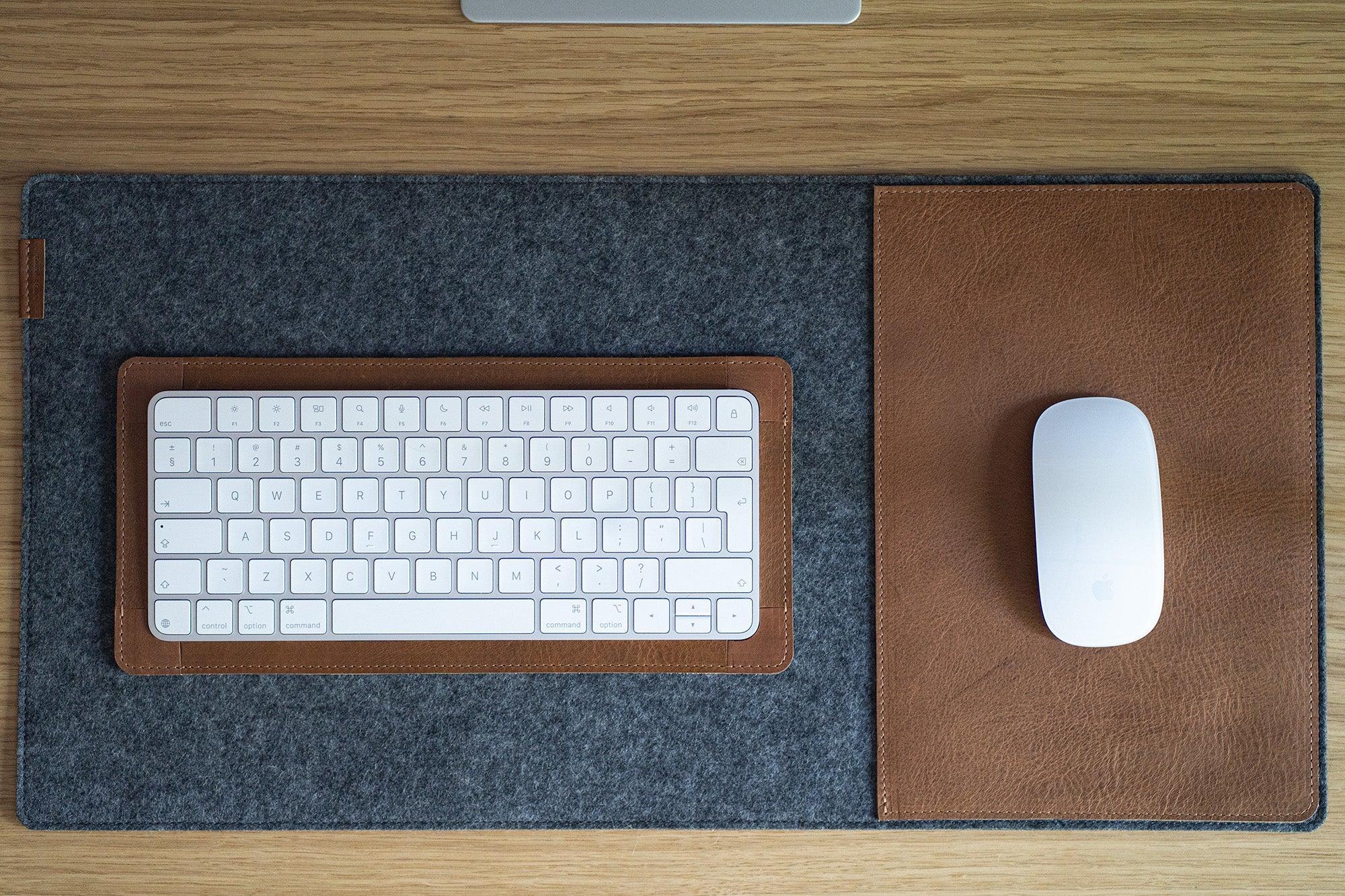 Apple Magic Keyboard in a brown leather tray on a grey felt desk pad; Magic Mouse on matching leather mouse area