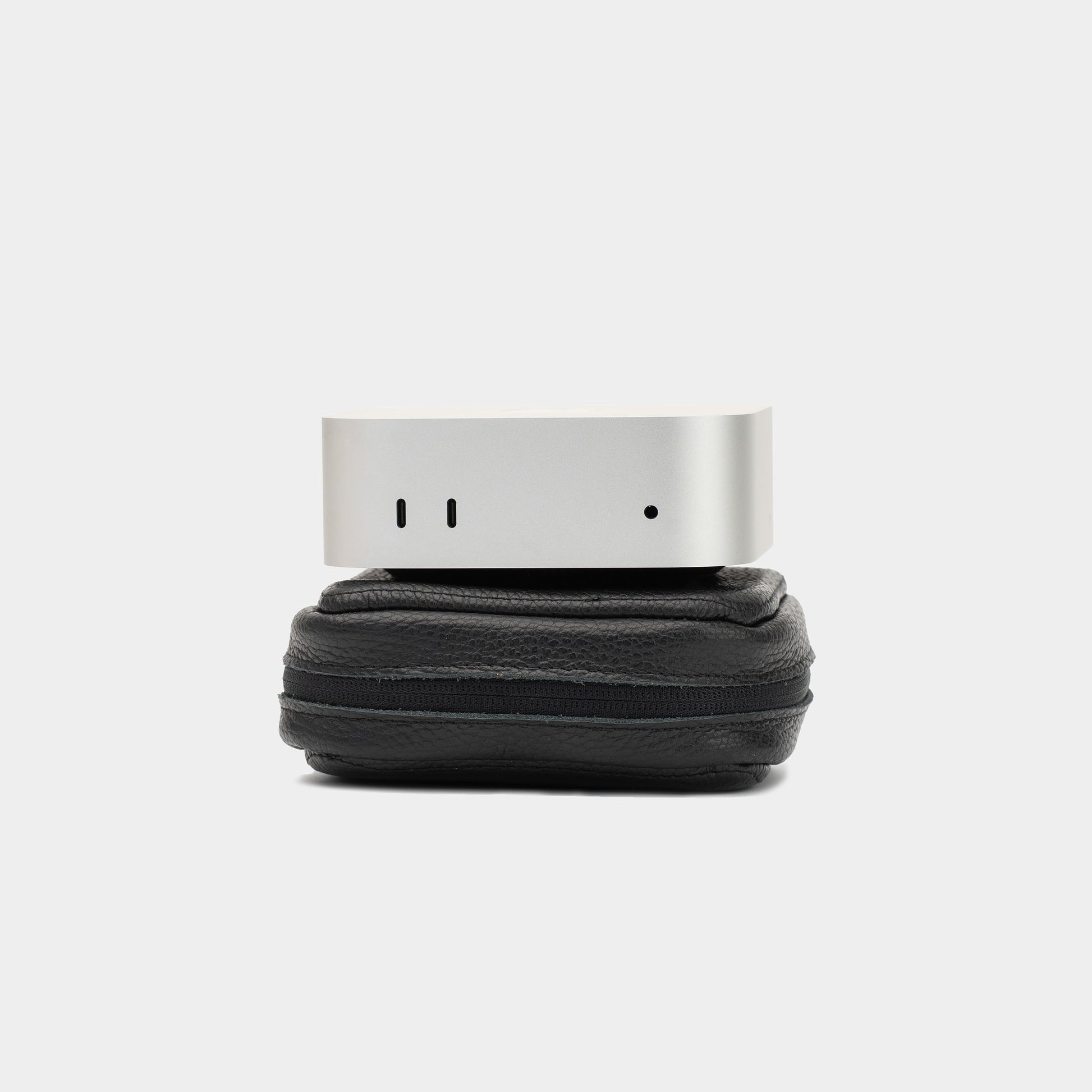 Mac Mini resting on a closed black flat-grain leather case, showing the compact side profile and zip-around edge