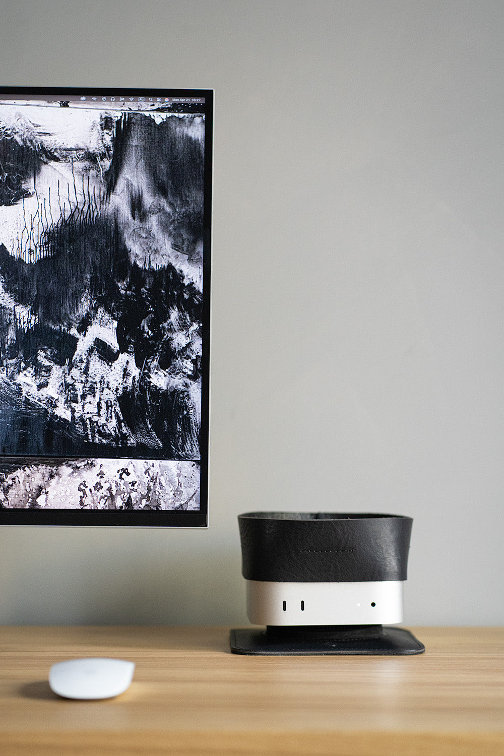 Black leather tray mounted on Mac Mini beside monitor and Magic Mouse on wooden desk, shown in full workspace setup