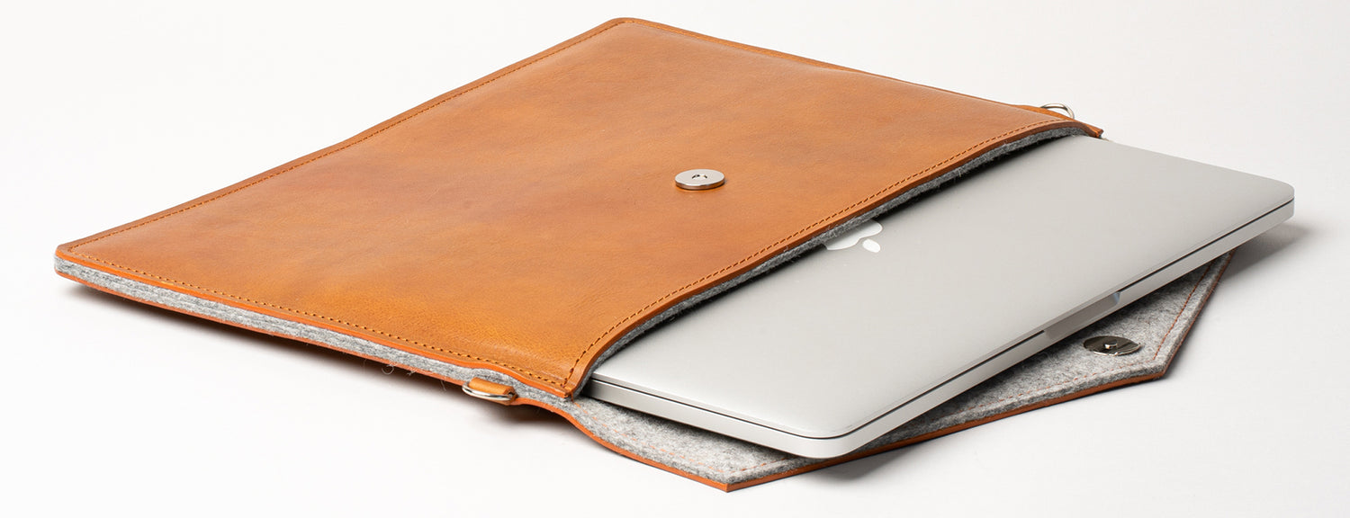 the photo of macbook in leather sleeve bag made from premium Italian leather in cognac brown color with gray wool felt