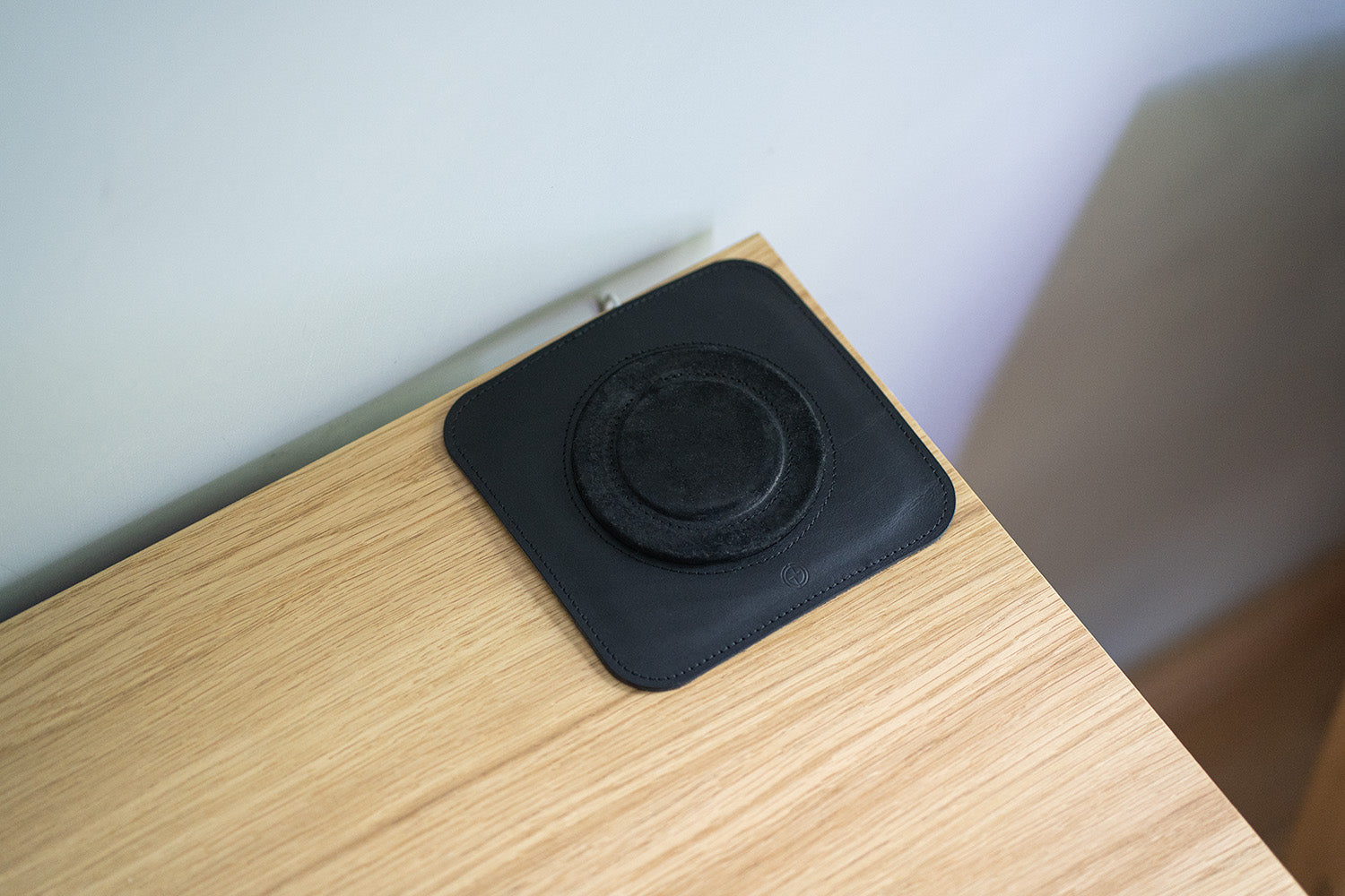 Black leather MagSafe charging mat on wooden desk, shown empty with circular felt MagSafe insert visible