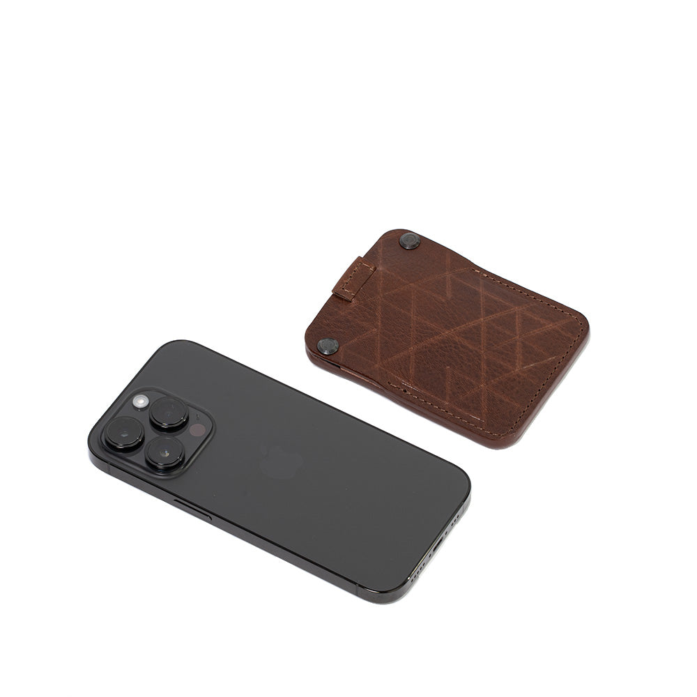 a photo which compare dimensions of the best AirTag card holder for men and woman made from brown premium Italian leather by Geometric Goods with iPhone 14 pro