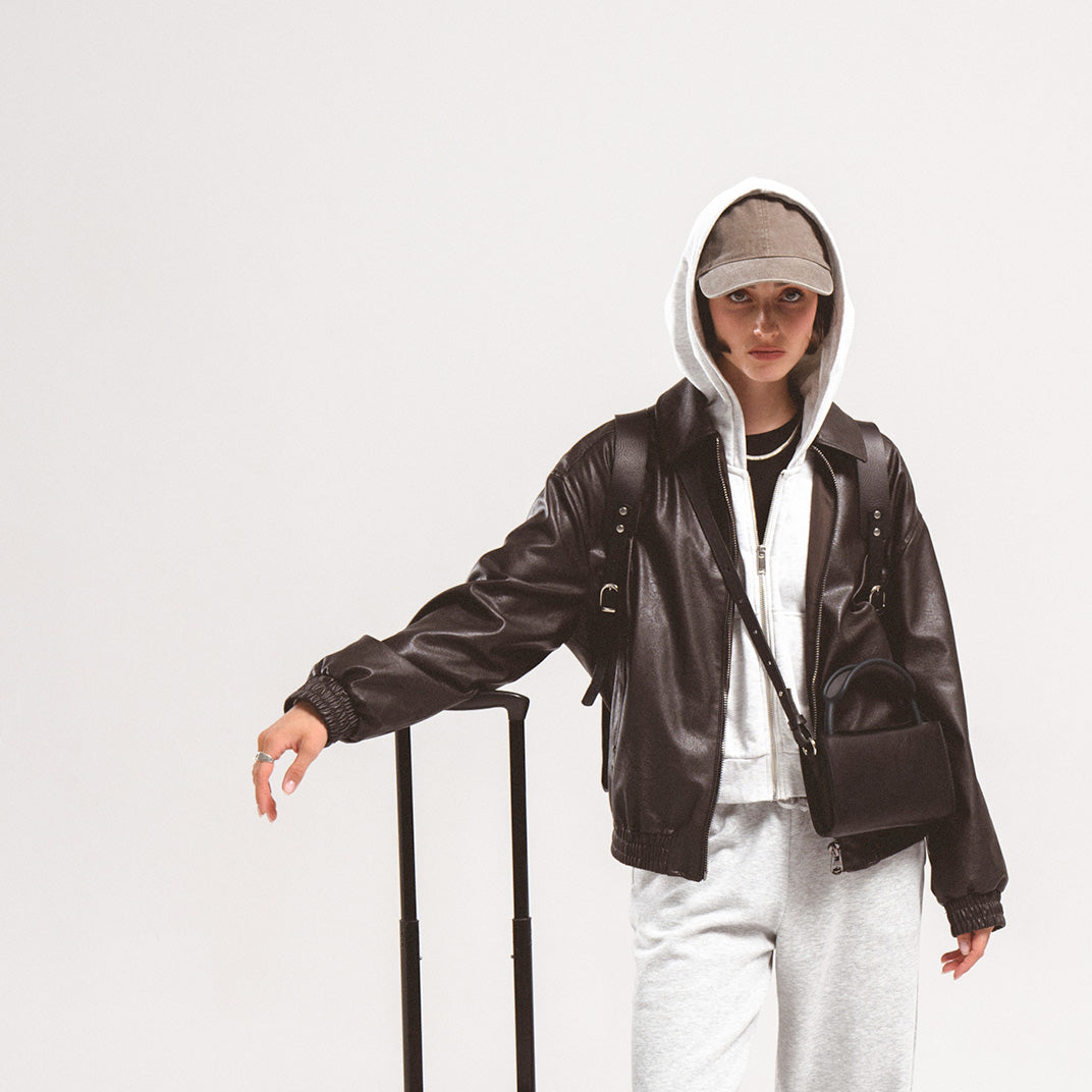 Leather case for AirPods Max featured on a young traveler in a leather jacket and hoodie, posing with a suitcase.