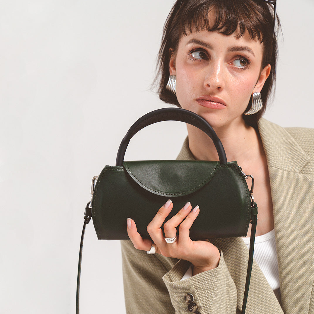 Leather case for AirPods Max in elegant green, held closely by a young woman in a chic blazer, showcasing a modern accessory