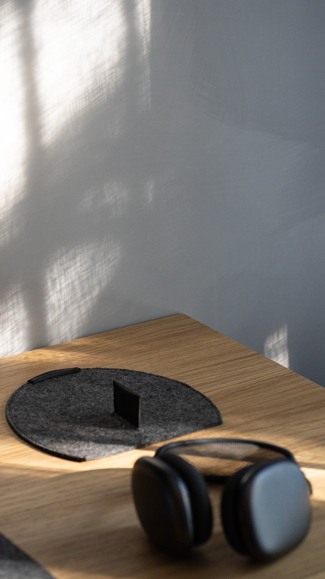 Grey wool felt AirPods Max rest station with leather magnetic tab on a wooden desk; AirPods Max in the foreground.