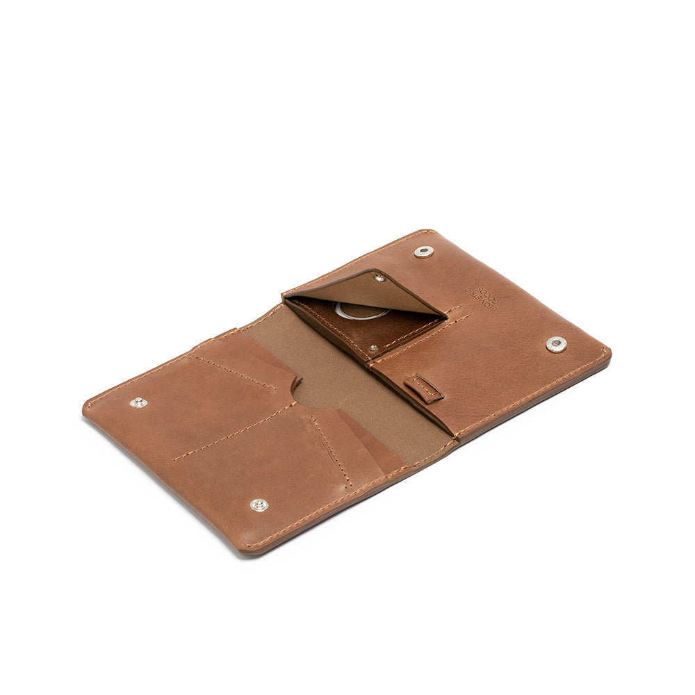 An image of a brown leather AirTag travel wallet from Geometric Goods, closed and laying flat on a surface. The wallet features multiple card slots and a hidden compartment for an AirTag device. The exterior of the wallet is made from premium Italian vegetable-tanned leather.